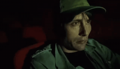 A Man Wearing A Hat Is Sitting In A Dark Room . GIF