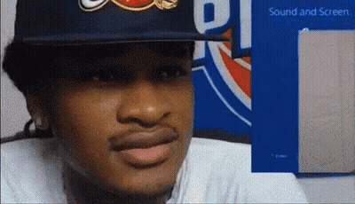 A Man Wearing A Hat Is Sitting In Front Of A Sign That Says ' Sound And Screen ' GIF