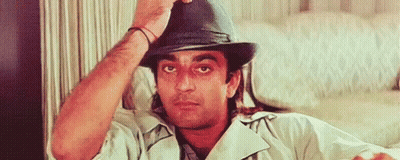 A Man Wearing A Hat Is Sitting On A Couch And Adjusting His Hat . GIF