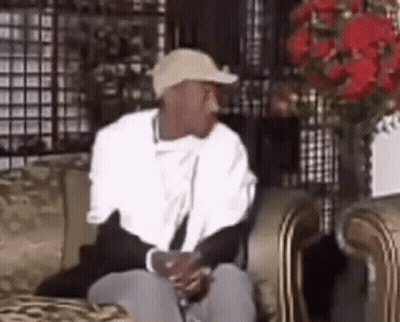 A Man Wearing A Hat Is Sitting On A Couch . GIF