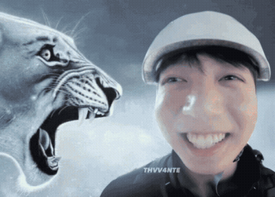 A Man Wearing A Hat Is Smiling In Front Of A Lion GIF