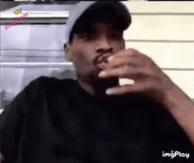 A Man Wearing A Hat Is Smoking A Cigarette While Looking At His Phone . GIF