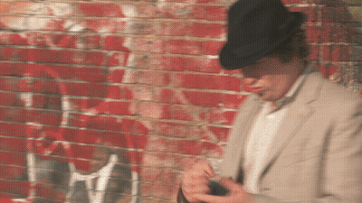 A Man Wearing A Hat Is Standing In Front Of A Brick Wall GIF