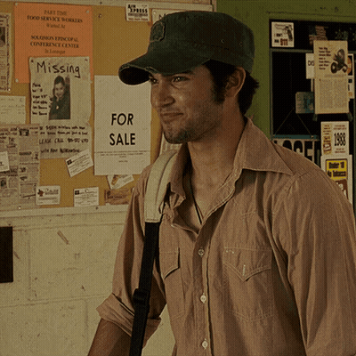 A Man Wearing A Hat Is Standing In Front Of A Bulletin Board With Missing And For Sale Signs On It GIF