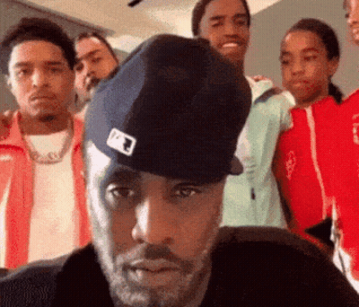 A Man Wearing A Hat Is Standing In Front Of A Group Of Men . GIF