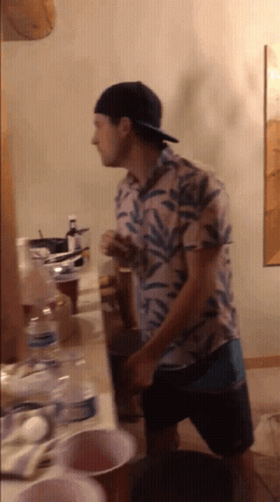 A Man Wearing A Hat Is Standing In Front Of A Table GIF