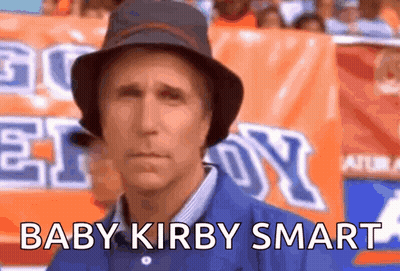 A Man Wearing A Hat Is Standing In Front Of An Orange Sign That Says Baby Kirby Smart GIF