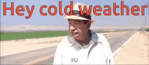 A Man Wearing A Hat Is Standing On The Side Of A Road With The Words Hey Cold Weather Written Above Him GIF
