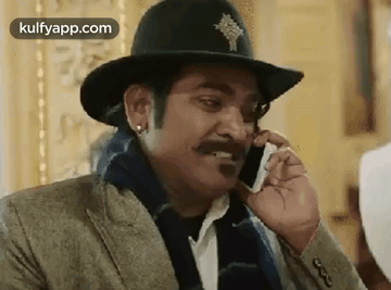 A Man Wearing A Hat Is Talking On A Cell Phone . GIF