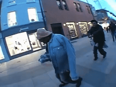 A Man Wearing A Hat Is Walking Down A Sidewalk In Front Of A Store That Says James GIF