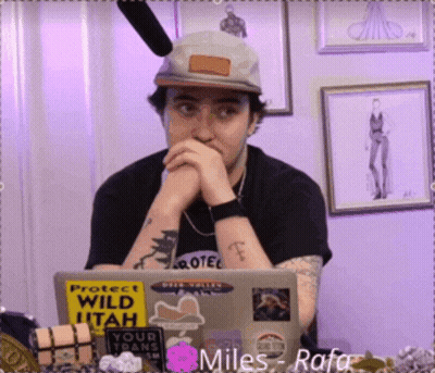 A Man Wearing A Hat Sits In Front Of A Laptop With Stickers On It Including One That Says Protect Wild Utah GIF