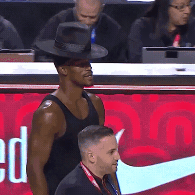 A Man Wearing A Hat Stands In Front Of A Red Nike Sign GIF