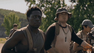 A Man Wearing A Hat Stands Next To Another Man In A Long Walk Advertisement GIF