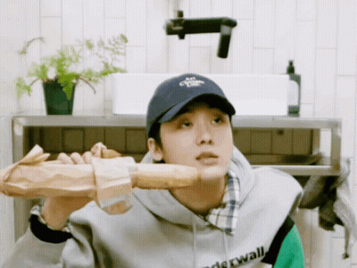 A Man Wearing A Hat That Says " Air " On It Holds A Loaf Of Bread Over His Shoulder GIF