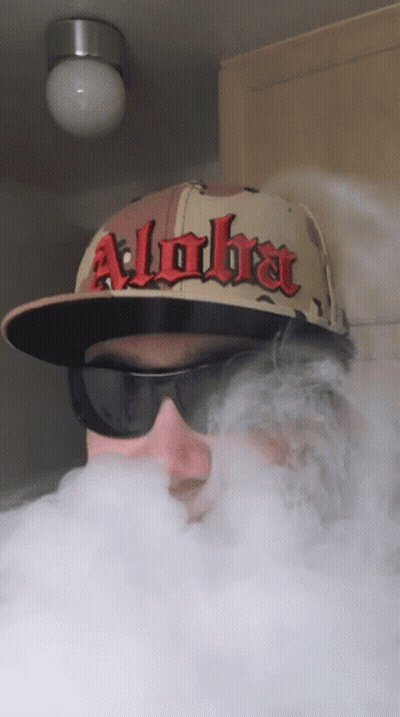 A Man Wearing A Hat That Says Alpha Is Blowing Smoke GIF