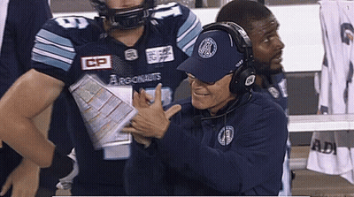A Man Wearing A Hat That Says Argonauts Talks To A Football Player GIF