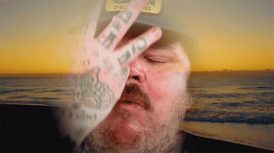 A Man Wearing A Hat That Says Cycles Covers His Face With His Hand GIF