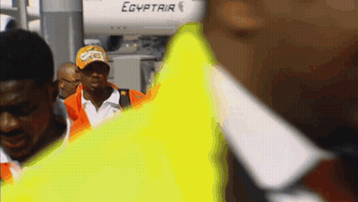 A Man Wearing A Hat That Says ' Egyptair ' On It Walks In Front Of An Airplane GIF