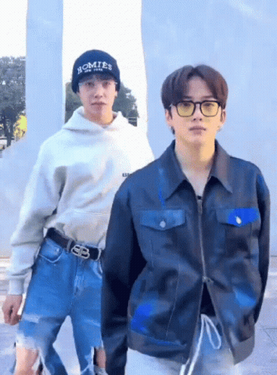 A Man Wearing A Hat That Says Homies On It Is Standing Next To Another Man Wearing A Jacket . GIF