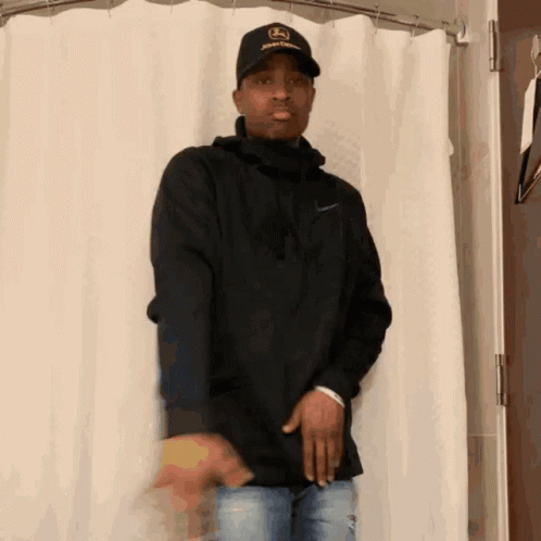 A Man Wearing A Hat That Says John Deere On It Stands In Front Of A Shower Curtain GIF