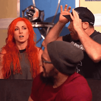 A Man Wearing A Hat That Says ' Nbc ' On It Stands Next To A Woman With Red Hair GIF