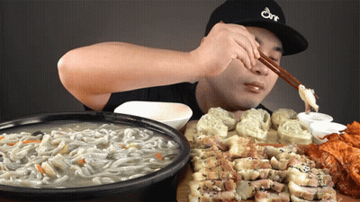 A Man Wearing A Hat That Says One Is Eating Noodles GIF