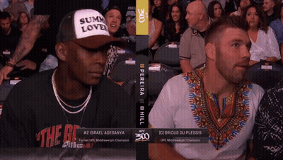 A Man Wearing A Hat That Says Sum Love Sits Next To A Man Wearing A Shirt That Says The G GIF