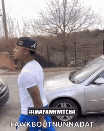 A Man Wearing A Hat With The Letter A On It Is Walking Down A Street GIF