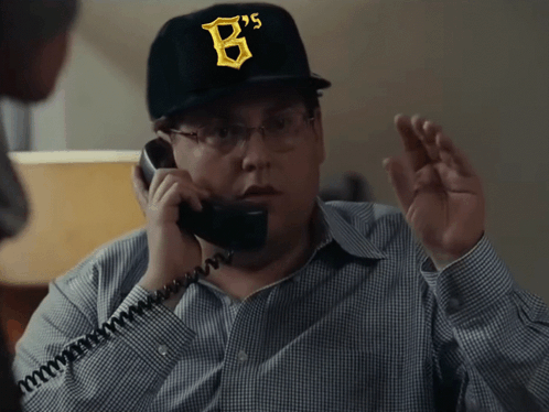 A Man Wearing A Hat With The Letter B On It Talks On A Phone GIF