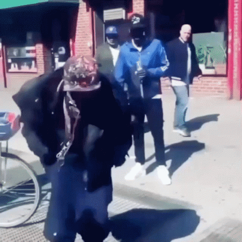 A Man Wearing A Hat With The Letter S On It Walks Down The Street GIF