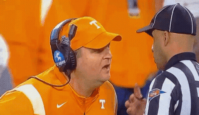 A Man Wearing A Hat With The Letter T On It Is Talking To A Referee On A Football Field . GIF