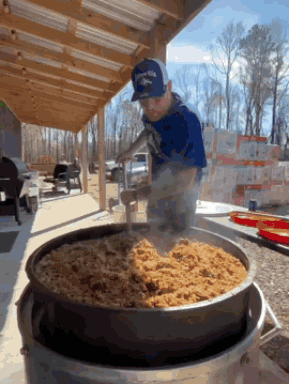 A Man Wearing A Hat With The Word Eagles On It Stirs A Large Pot Of Food GIF