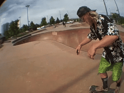 A Man Wearing A Hawaiian Shirt And Green Shorts Rides A Skateboard GIF