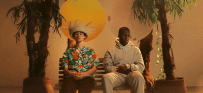 A Man Wearing A Hawaiian Shirt Sits Next To Another Man Wearing A White Hoodie GIF