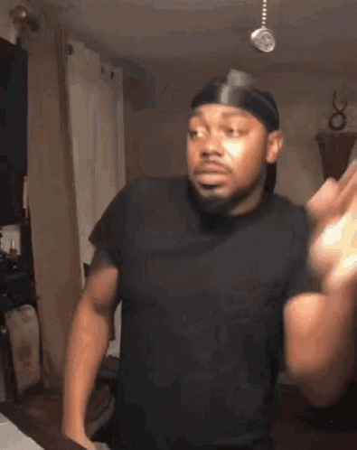 A Man Wearing A Headband And A Black Shirt Is Standing In A Living Room With His Arms Outstretched . GIF