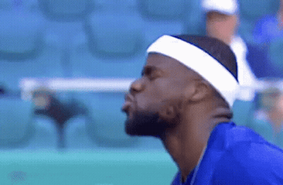A Man Wearing A Headband And A Blue Shirt Is Blowing A Kiss At The Camera . GIF