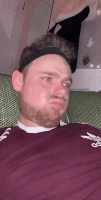 A Man Wearing A Headband And A Maroon Adidas Shirt Is Sitting On A Couch . GIF
