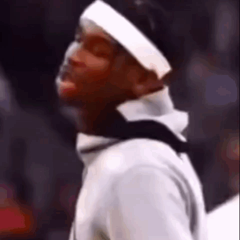 A Man Wearing A Headband And A White Shirt Is Standing In Front Of A Crowd Of People . GIF