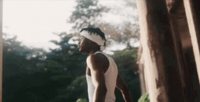 A Man Wearing A Headband And A White Tank Top Is Standing In Front Of A Tree . GIF