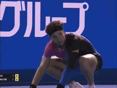 A Man Wearing A Headband And A Wristband Is Standing In Front Of A Blue Sign . GIF
