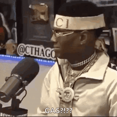 A Man Wearing A Headband And Glasses Is Sitting In Front Of A Microphone And Talking Into It . GIF
