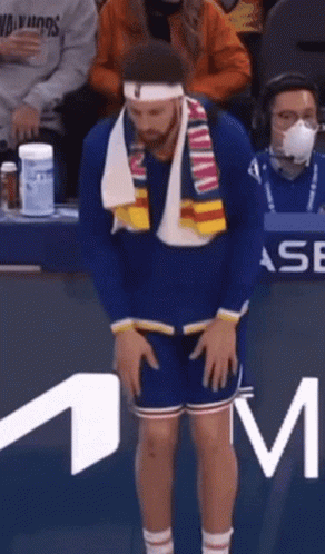 A Man Wearing A Headband And Scarf Is Standing In Front Of A M Logo GIF