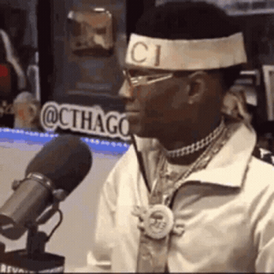 A Man Wearing A Headband And Sunglasses Is Sitting In Front Of A Microphone . GIF