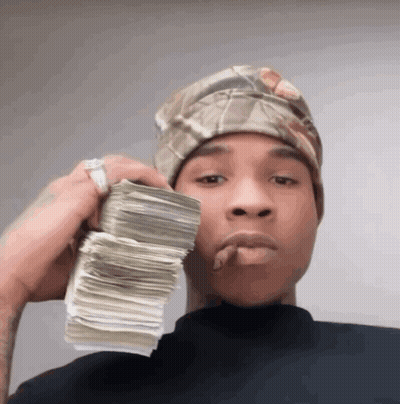 A Man Wearing A Headband Holds A Stack Of Money In His Hand GIF
