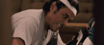 A Man Wearing A Headband Is Smiling While Looking At A Pair Of Shoes . GIF