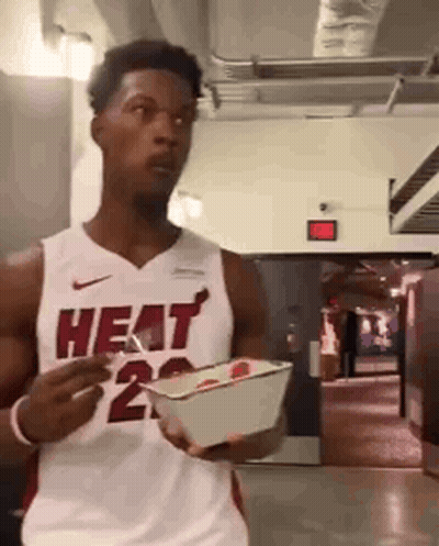 A Man Wearing A Heat Jersey Is Holding A Box Of Food GIF