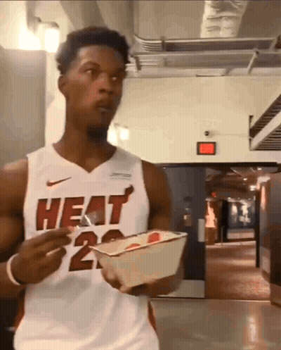 A Man Wearing A Heat Jersey Is Holding A Container Of Food GIF