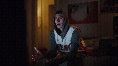 A Man Wearing A Heat Jersey Sits On A Bed At Night GIF