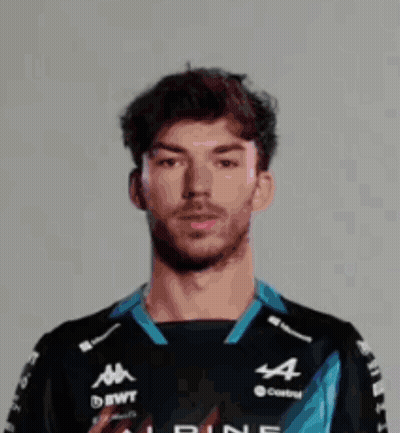 A Man Wearing A Helmet And A Castrol Shirt Is Standing In Front Of A White Wall . GIF