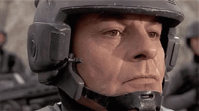 A Man Wearing A Helmet And A Mask Is Looking At The Camera . GIF